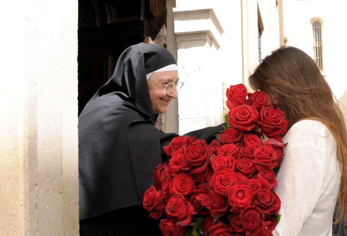 La priora del monastero di Santa Rita da cascai con un mazzo di rose in mano e una donna di profilo