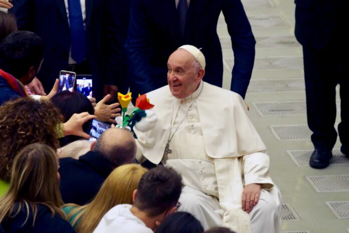 Papa francesco seduto sulla sedia a rotelle saluta i presentiin piazza