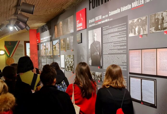 Alcuni visitatori di spalle in visita ad una delle stanze del museo della memoria con i pannelli e le foto