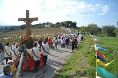 La processione di spalle con in primo piano il ìSS Crocifisso e la tanta gente che cammina lunga una strada di campagna