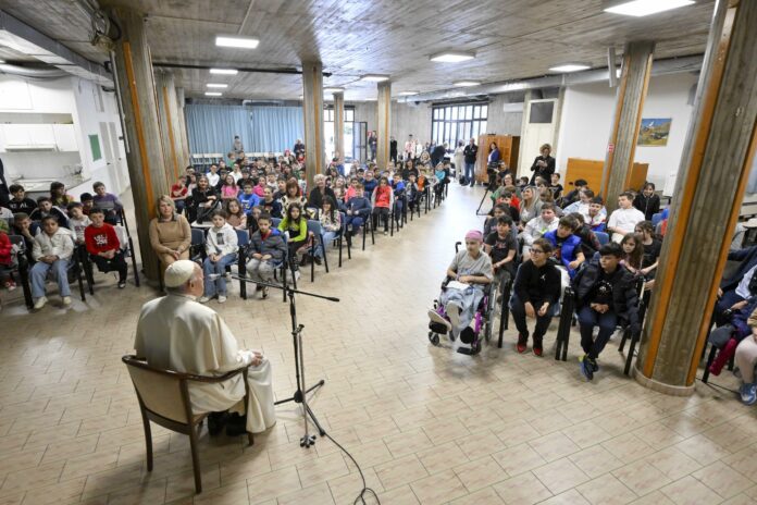 Papa Francesco seduto sulla sedia di spalle, davanti a se ha dei bambini seduti sulle panche all'interno di una chiesa di Roma