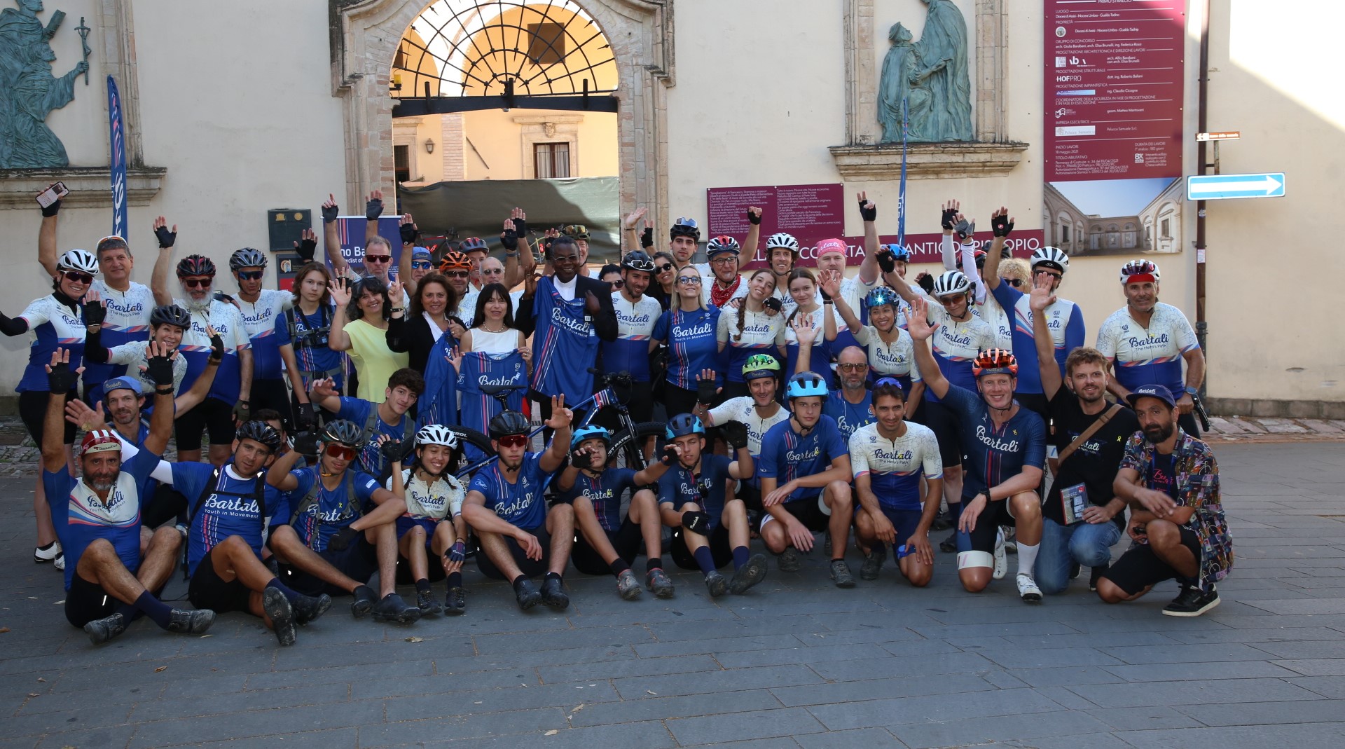 Foto di gruppo dei ciclisti davanti all'ingresso del vescovado dove si trova il museo della memeoria di Assisi