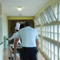 Un agente della polizia penitenziaria di spalle mentree spinge un carrello in un corridoio del carcere con a destra delle finestre