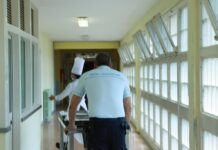 Un agente della polizia penitenziaria di spalle mentree spinge un carrello in un corridoio del carcere con a destra delle finestre