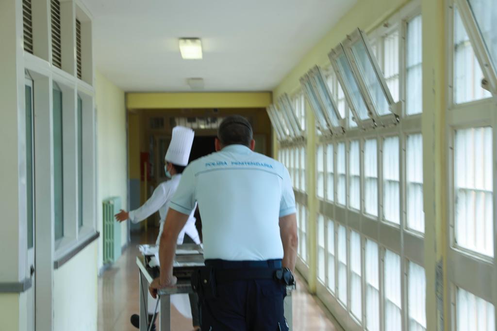 Un agente della polizia penitenziaria di spalle mentree spinge un carrello in un corridoio del carcere con a destra delle finestre