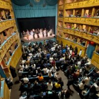 Tanti giovani seduti sulle poltronicine del Teatro e sui palchetti, sul palco i frati minori