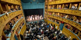 Tanti giovani seduti sulle poltronicine del Teatro e sui palchetti, sul palco i frati minori