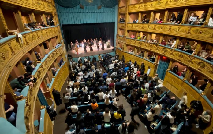 Tanti giovani seduti sulle poltronicine del Teatro e sui palchetti, sul palco i frati minori