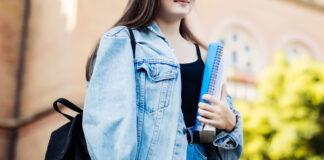 una ragazza ripresa di fronte, conm la testa visibile a metà, con in mano un qiuaderno e sulle spalle uno zaino nero