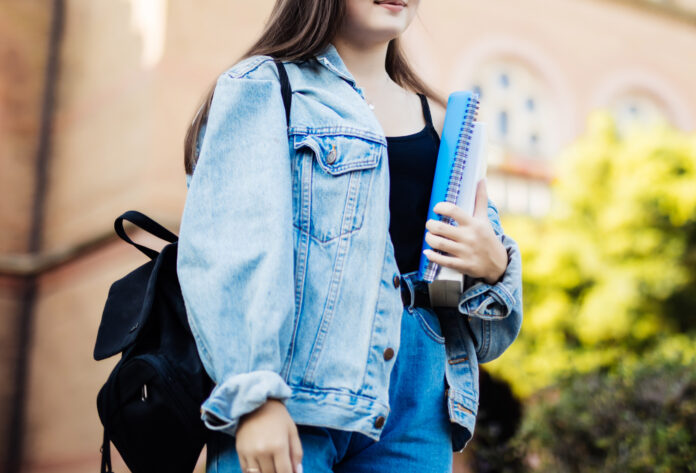 una ragazza ripresa di fronte, conm la testa visibile a metà, con in mano un qiuaderno e sulle spalle uno zaino nero