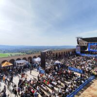 La piazza Inferiore della Basilica di Assisi con le persone sedute sulle sedie davanti al palco, veduta dall'alto