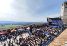 La piazza Inferiore della Basilica di Assisi con le persone sedute sulle sedie davanti al palco, veduta dall'alto