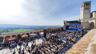 La piazza Inferiore della Basilica di Assisi con le persone sedute sulle sedie davanti al palco, veduta dall'alto