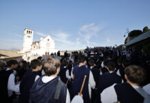 pellegrini di spalle sullo sfondo la basilica superiore di San Francesco ad Assisi