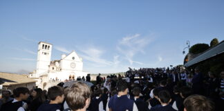 pellegrini di spalle sullo sfondo la basilica superiore di San Francesco ad Assisi