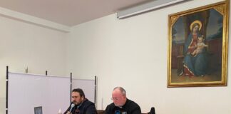 Don Francesco Verzini a sinistra e a destra don Fabio Rosini seduti dietro ad un tavolo, visti di tre quarti e alle spalle un quadro con ritratto la Madonna con il Bambino