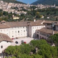 Veduta dall'alto del Seminario regionale umbro immerso nella vegetazione, sullo sfondo Assisi