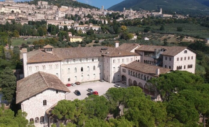 Veduta dall'alto del Seminario regionale umbro immerso nella vegetazione, sullo sfondo Assisi